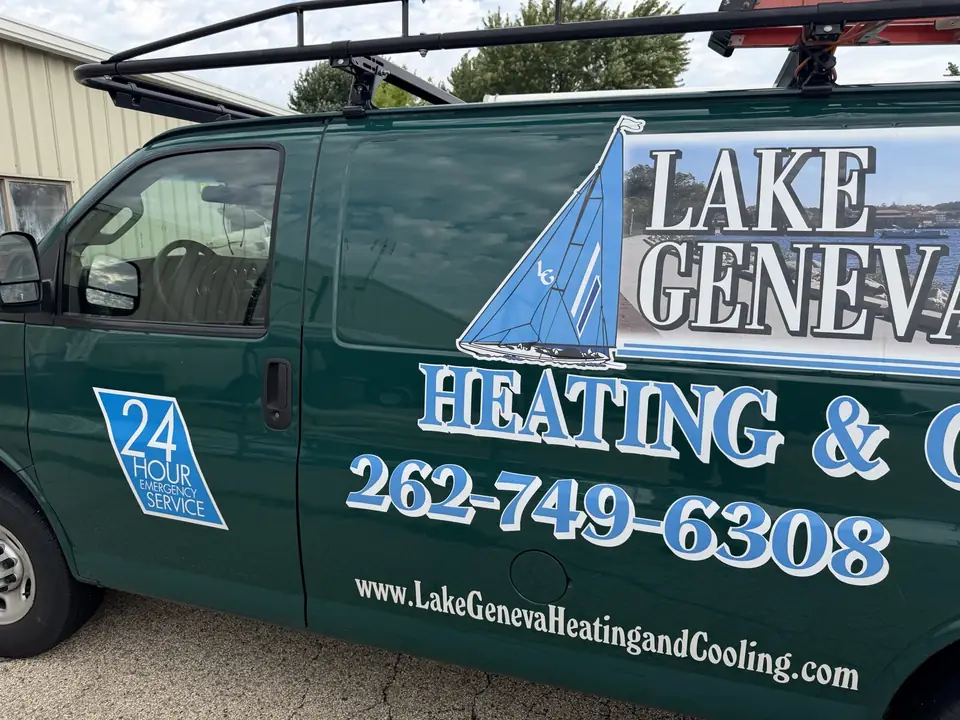 Driver side of the green Lake Geneva Heating and Cooling van, with the sailboat logo, a 24 Hour Emergency Service badge on the door and the phone number 262-749-6308 across the side panel