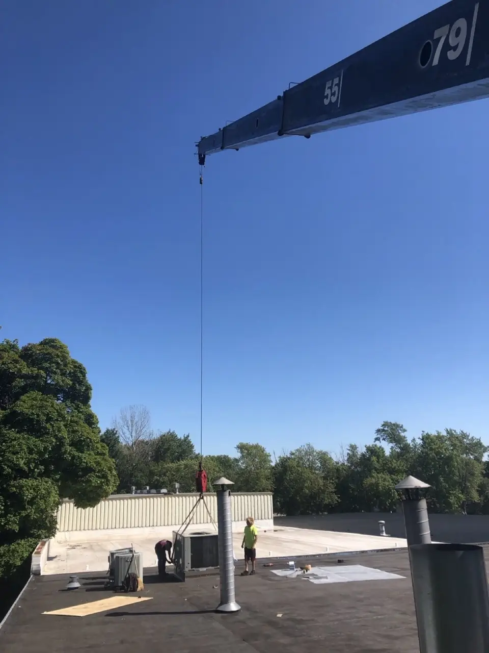 Crane boom and crew rigging a rooftop unit on a flat roof